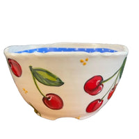 A handcrafted ceramic bowl with a soft blue interior, featuring a cherry blossom design on a white background. The bowl has a fluted edge and a handle on the side.