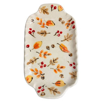 An oval ceramic serving platter with scalloped edges, decorated with a hand-painted autumn pattern of orange and yellow leaves, brown acorns, and red berries on a cream background.